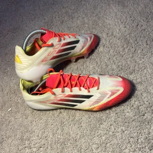 Adidas X F50 fotbollsskor - Säljer ett par Adidas F50 elite pure victory fotbollsskor i vitt med röda och svarta detaljer. Skorna har snörning och en lätt, strömlinjeformad design med mönstrad ovandel och låg profil. Perfekta för dig som vill ha snabba fötter på planen. Skorna är använda 10-15 gånger och är i storleken 41/3 skorna passar alla typer av fötter och är super lätta vilket gör att man rör sig snabbare och springer snabbare. Skorna är i elite och kommer även i en påste. Original pris är 3099kr.Pris kan diskuteras