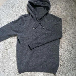 Mörkgrå merinoull hoodie - Mysig mörkgrå stickad hoodie med huva och dragsko. Tröjan har långa ärmar och är perfekt för kyligare dagar. Enkel och stilren design som passar till det mesta. MERINOULL!!