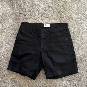 Svarta shorts från These Glory Days - Svarta shorts från These Glory Days med klassisk design. De har knapp och dragkedja framtill, bälteshällor och två bakfickor. Perfekta för en stilren och enkel look.