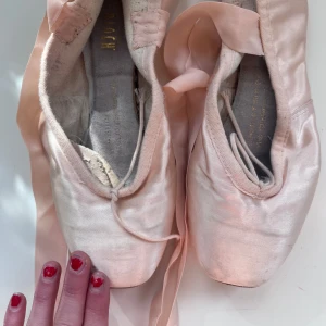 Rosa tåspets balettskor med satinband - Säljer ett par klassiska rosa balettskor från Suprima i satin med långa band att knyta runt vristen. Skorna har rund tå och platt sula, perfekta för balettträning eller uppvisning.