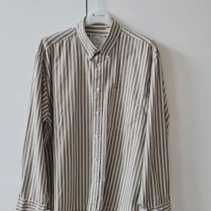 Randig skjorta från No1 Shirts strl L (herr) - Säljer en klassisk skjorta från No1 Shirts i beige och vitt med vertikala ränder. Skjortan har lång ärm, knappar framtill och en bröstficka. Tillverkad i 100% bomull. Bröstmått 120cm. Storlek L. Kan hämtas i Vallentuna.