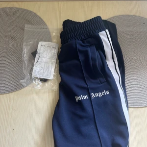 Palm Angels blå träningsbyxor med vita ränder - Säljer ett par mörkblå byxor från Palm Angels. Köpta på NK i Stockholm kvitto följer med. Byxorna är använda men som i nyskick. Mer bilder så fråga bara så löser vi😃pris diskuterbart