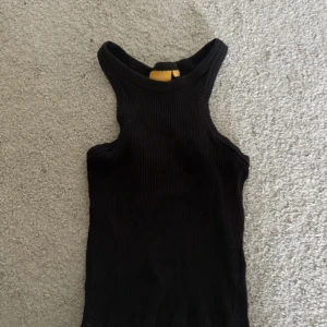 Svart ribbad linnetopp från Gina Tricot - Säljer en svart ribbad linnetopp från Gina Tricot. Toppen är ärmlös med rund halsringning och har en tight passform. Perfekt att styla till jeans eller kjol.