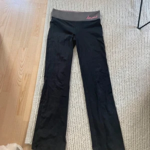 Svarta yogabyxor från Victoria's Secret PINK - Svarta yogabyxor från Victoria's Secret PINK med grå och rosa midja där det står 'Love Pink'. Byxorna har bootcut-modell och är perfekta för träning eller yoga. Mjukt och stretchigt material för maximal komfort.