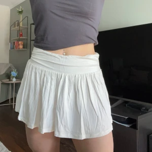 Vit kortkjol från Nelly - Säljer en vit kortkjol från Nelly med bred resår i midjan och lätt rynkad kjol🤍 Kjolen har en luftig och flowy passform som ger en avslappnad känsla. Perfekt att styla med en enkel topp eller hoodie. Använd en gång