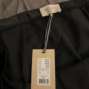 Svart satinlångkjol från Freequent - Säljer en svart långkjol i satin från Freequent. Kjolen har en elegant glansig yta och rak passform som faller snyggt längs kroppen. Helt oanvänd med prislapp kvar. Den har en dragkedja på sidan och resår i midjan. Nypris är 399kr.🌸 