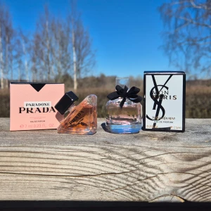 Prada Paradoxe och Yves Saint Laurent Mon Paris - Två exklusiva miniparfymer: Prada Paradoxe (7 ml) i en unik trekantig flaska med ljusrosa doft och svart kork, samt Yves Saint Laurent Mon Paris (7,5 ml) i en rund flaska med svart rosett och transparent vätska. Båda kommer i sina originalkartonger. Endast doftade på.
