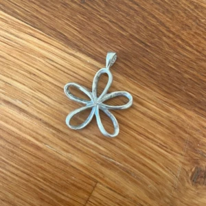 Äkta silver, blommigt hänge - Säljer ett stilrent hänge i form av en blomma med fem rundade kronblad. Hänget är i äkta silver och har en enkel ögla för kedja. Perfekt för att ge din look en söt och unik touch.