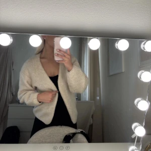 Beige stickad kofta - Mysig beige stickad kofta med lång ärm och avslappnad passform. Perfekt att slänga över en topp för en enkel och stilren look. Koftan har en öppen front och är superenkel att matcha med olika outfits.