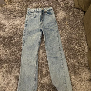 Ljusblå raka jeans från STR - Säljer ett par ljusblå jeans från STR med klassisk femficksdesign och raka ben. Jeansen har normal passform och stängs med knapp och dragkedja. Perfekta till vardags för en avslappnad stil.