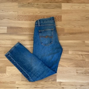 Blå jeans från Nudie Jeans - Säljer ett par klassiska blå jeans från Nudie Jeans med fem fickor och normal passform. Jeansen har en snygg tvätt och detaljerade sömmar på bakfickorna. Perfekta för dig som gillar tidlös stil och bra kvalitet.