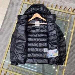 Svart dunjacka från Moncler - Säljer en svart, glansig dunjacka från Moncler med hög krage och avtagbar huva. Jackan har dragkedja framtill, två fickor med dragkedja och Moncler-logga på ärmen. Perfekt för kyliga dagar.