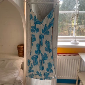 Vit och blå boho sommarklänning  - Säljer en vit klänning med blått paisleymönster och smala axelband. Det står att det är en storlek L men den är för liten för mig och jag har storlek m. Klänningen har v-ringning och är ärmlös, perfekt för varma dagar. Resår i ryggen för skön passform. Lätt och luftig modell som passar till sommaren.