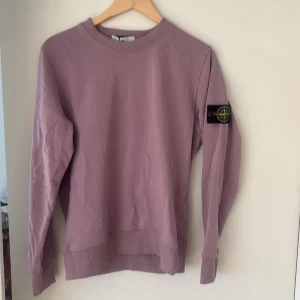 Ljuslila sweatshirt från Stone Island - Säljer en ljuslila sweatshirt från Stone Island med klassisk patch på ärmen. Tröjan har rund halsringning, långa ärmar och ribbade muddar. Perfekt för en avslappnad och stilren look.