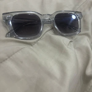 Chimi - Snygga solglasögon med transparent båge och fyrkantig form. Glasen är gråtonade och ger en cool look. Perfekta för att lyfta din stil under soliga dagar. Har tyvärr inte fodralet kvar