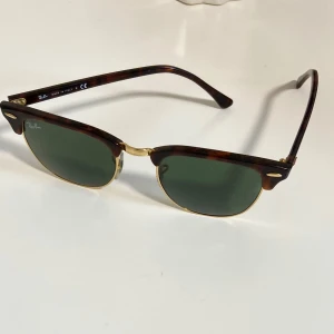 Ray-Ban Clubmaster solglasögon - Klassiska Ray-Ban Clubmaster solglasögon med brunsköldpaddsmönstrad båge, guldiga detaljer och gröna glas. Snygg retrostil som passar till många tillfällen. Modell RB3016, tillverkade i Italien.