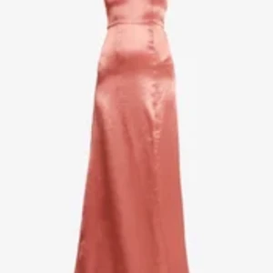 Rosa långklänning med smala axelband - Elegant rosa långklänning med smala axelband och en subtil slits framtill. Klänningen har en v-ringad design och är tillverkad i ett glansigt material som ger en lyxig känsla. Perfekt för speciella tillfällen. Uppsydd längst ner men lång nog för att ha klackar i om man är 174 som jag.