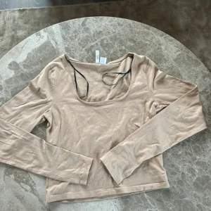 Beige långärmad topp  - En beige långärmad baströja med en djup halsringning från H&M som är väldigt enkel att styla och fin att ha på sig med ett par jeans. Tröjan är i storlek S och är cropped typ. Liten i storleken, passar även XS.