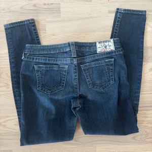Mörkblå jeans från True Religion W28💙 - Säljer ett par mörkblå jeansbyxor från True Religion med dekorativa nitar på bakfickorna och klassisk logga på linningen. Byxorna har normal passform. 