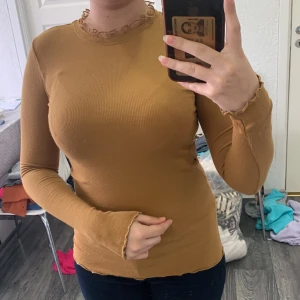 Mustardfärgad ribbad långärmad topp från Name It - Säljer en snygg senapsgul ribbad topp från Name It. Tröjan har lång ärm, tight passform och vågiga kanter vid hals och ärmslut. Perfekt att styla med jeans eller kjol för en trendig look.