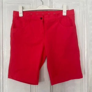 Röd rosa shorts från Crivit - Snygga röd rosa shorts från Crivit med klassisk femficksdesign och normal passform. Tillverkade i polyester och elastan för en bekväm känsla. Perfekta för sommardagar och enkel att matcha med olika toppar.