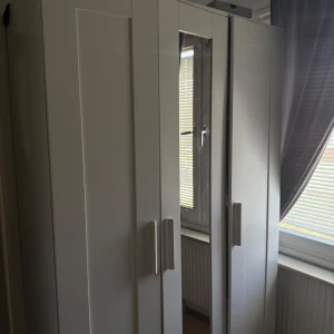 Vit garderob med spegeldörr - Säljer en stilren vit garderob med tre dörrar, varav en har en helkroppsspegel. Garderoben har raka linjer och moderna handtag i vitt. Perfekt för att organisera kläder och accessoarer i sovrummet.