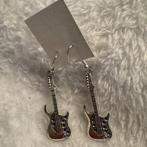 Silverfärgade gitarrörhängen - Coola örhängen i form av elgitarrer i silverfärg. Perfekta för dig som älskar musik och vill sticka ut med din stil. Hängande modell med fina detaljer på gitarrerna. Krokarna är i sterling silver 