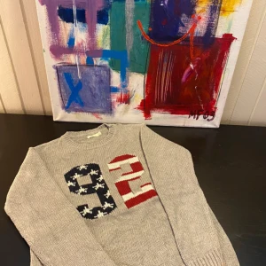 Grå stickad tröja - Säljer en grå stickad tröja med stora siffror 9 och 4 framtill, där ena siffran är mönstrad i svart och vit och den andra i rött och vitt.