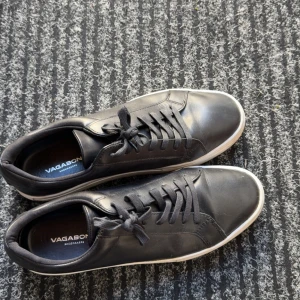 Svarta sneakers från Vagabond - Säljer ett par stilrena svarta sneakers från Vagabond med snörning och vit sula. Skorna är i skinn och har en klassisk rund tå. Perfekta för dig som gillar enkel och tidlös design.
