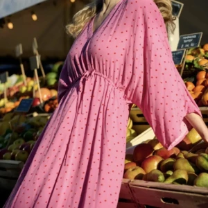 Rosa prickig långklänning från Culture - Säljer en rosa långklänning från Culture med röda prickar och v-ringning. Klänningen har trekvartsärm och knyt i midjan för en avslappnad passform. Tillverkad i EcoVero-material som känns mjukt och luftigt.