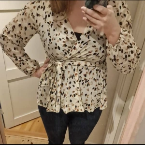 Mönstrad omlottblus med knytband - Säljer en beige omlottblus med svart och brunt prickigt mönster. Använd max fyra gånger och priset kan diskuteras. 