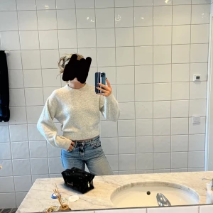 Ljusgrå stickad tröja - Mysig ljusgrå stickad tröja med rund halsringning och långa ärmar. Tröjan har en klassisk passform och ribbade muddar vid ärmslut och nederkant.