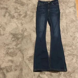 Blå bootcut jeans från NLY Jeans - Snygga mörkblå bootcut jeans från NLY Jeans med klassisk femficksdesign och kontrastsömmar. Jeansen har hög midja och är tillverkade i stretchigt denim för en bekväm passform. Perfekta för dig som gillar en retroinspirerad look.