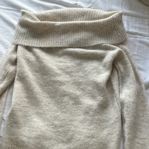 Beige offshoulder stickad tröja Gina Tricot - Supermysig beige stickad tröja från Gina Tricot med bred ribbad offshoulder-krage. Perfekt för lager-på-lager och chill höst- eller vinterstil. Långärmad och i mjukt material som känns skönt mot huden.