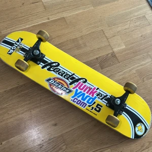 skateboard - Bilderna visar en skateboard med gul och svart design, dekorerad med flera klistermärken och tydliga tecken på användning. Ingen bok syns på bilderna.