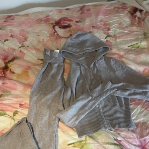 Grå stickade mjukisbyxor S - Mysiga grå mjukisbyxor i stickad kvalitet med bred ribbad midja och justerbart bälte i midjan. Byxorna är tillverkade i en mjuk mix av viskos, polyester och polyamid. Perfekta för chill dagar hemma eller när du vill vara extra bekväm.