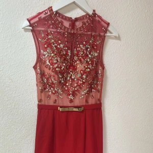 Röd långklänning med paljetter och pärlor - Supersnygg röd långklänning med transparent mesh upptill, dekorerad med glittrande paljetter, pärlor och broderade blommor. Klänningen är ärmlös och har ett elegant bälte med guldfärgad rosett i midjan. Perfekt för bal eller festliga tillfällen! Pris går att diskuteras vid smidigt köp ✨🤍