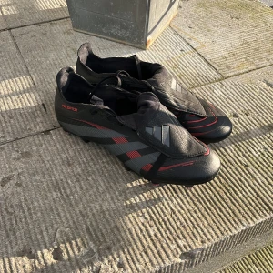 Adidas Predator fotbollsskor svart/röd - Säljer ett par Predator League Fold-over Tongue Soft Ground Fotbollsskor. Skorna har snörning, täckt plös och skruvdobbar för blöt gräsplan. Knappt använda och i fint skick. Alla dobbar är utbytta mot ett par bättre då de som ingick försvann på första träningen. Tveka inte vid frågor! Pris kan diskuteras vid snabb affär! Nypris: 1200 kr