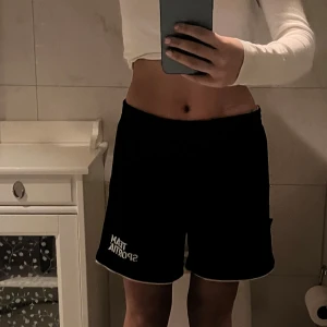 Svarta sportshorts från Team Sportia - Svarta sportshorts från Team Sportia med vit logga på vänster ben. De har en loose passform och elastisk midja. Perfekta för träning eller chill dagar. Tunt och lätt material med vit kant nertill för en clean look.