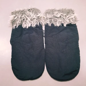 Svarta tumvantar med fuskpäls Point Zero strl 7,5 - Svarta tumvantar från Point Zero med fluffig gråvit fuskpäls vid handleden. Vantarna har en enkel, stilren design och är fodrade för extra värme. Perfekta för kalla vinterdagar när du vill hålla händerna varma och ändå se snygg ut.  Början till ett litet hål (se extra bild) annars fint skick