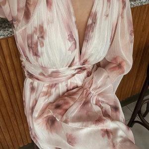 Ljus blommig omlottklänning med volang - Superfin eftertraktad kortklänning i ljusa toner med blommigt mönster och omlottliv. 