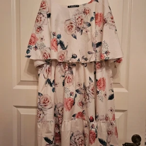 Blommig klänning från Sheilay XL - Romantisk klänning från Sheilay i ljus botten med stora blommor i rosa toner. Klänningen har volangdetaljer, lös passform. Perfekt för sommarens alla tillfällen. Materialet känns lätt och luftigt.   Hitta en dov fläck på magen och 2 små noppror längre ner på kjolen, syns knappt 
