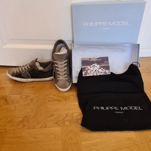 Grå Philippe Model sneakers. Limited Edition. - Snygga sneakers från Philippe Model i grått och svart med detaljer i mocka och skinn. Denna modell är Limited Edition. Originalbox, skopåse och äkthetsintyg följer med. Perfekta för dig som gillar stilrena och trendiga skor. Stolek 40 men är något små i storleken, passar även 39. Bra skick, inga hål eller skador. Sulan är såklart lite sliten men det finns mönster kvar, även lite rester från gammalt tuggummi under sulan (som går att ta bort), se bild.