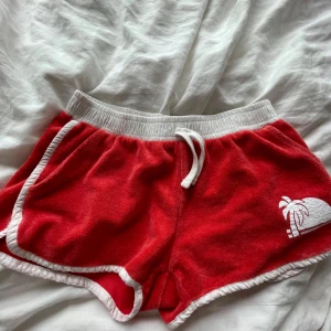 Röda frottéshorts med snörning - Röda shorts i mjuk frotté med vita detaljer och snörning i midjan. Perfekta för sommaren och chill dagar på stranden.