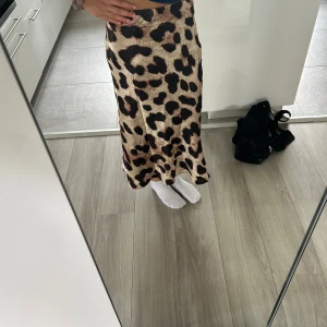 Leopardmönstrad långkjol i satin - Snygg långkjol med leopardmönster i beige, brunt och svart. Kjolen har en lätt glansig satinlook och sitter snyggt i midjan med en rak och flowy passform. Perfekt statement piece för dig som vill sticka ut. Passar även dig som har storlek xs 😊