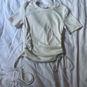 Ribbad vit topp med snörning - Superfin ribbad topp från Zara i vit färg. Modellen har korta ärmar och snörningsdetaljer på båda sidorna som du kan justera. 