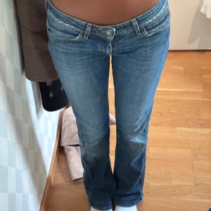 Blå Wrangler bootcut jeans låg midja - Säljer ett par snygga blå jeans med bootcut och låg midja. Jeansen har klassiska fickor och coola detaljer på bakfickorna. Perfekta för dig som gillar en avslappnad men trendig look.