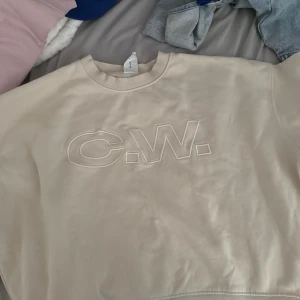 Beige sweatshirt från Carin Wester - Snygg beige sweatshirt från Carin Wester med broderad C.W.-logga framtill. Tröjan har rund halsringning, ribbade muddar och en relaxed passform. Perfekt för en chill och stilren look.