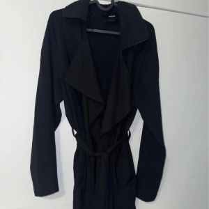 Svart trenchcoat med bälte - Stilren svart trenchcoat från Bik Bok med långa ärmar, bred krage och knytskärp i midjan. Storlek M. 