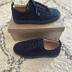 Mörkblå sneakers från Christian Louboutin  - Snygga mörkblå sneakers från Christian Louboutin i mocka med klassisk röd sula och diskret logga på insidan. Skorna har rund tå, snörning och en stilren design som passar perfekt till jeans eller dressat. Lyxig känsla med beige innersula och exklusiva detaljer.     OBS! kommer med lådan och Louboutine skohorn